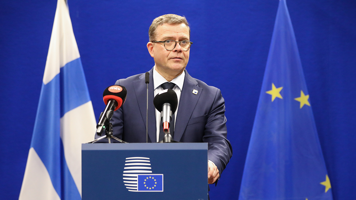 Pääministeri Opro puhuu tiedotustilaisuudessa puhujan korokkeella. Taustalla Suomen ja EU:n liput.
